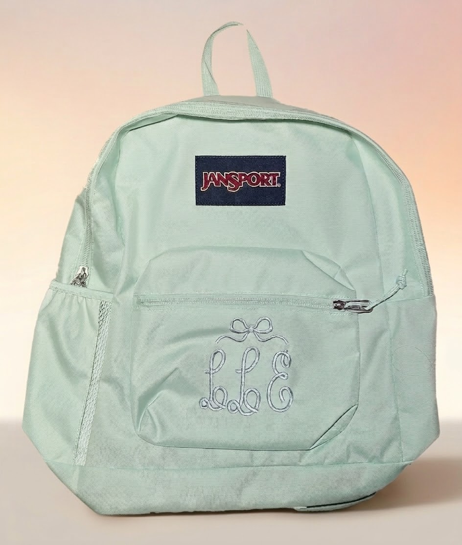 Mint green backpack with an embroidered script monogram and bow on the front pocket